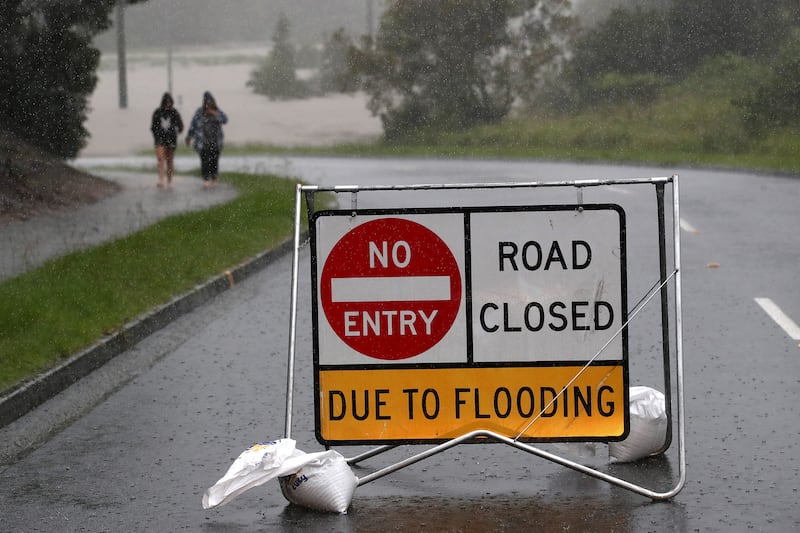 People walk in the rain past a sign warning the public about a road closure due to flooding, in Logan. EPA