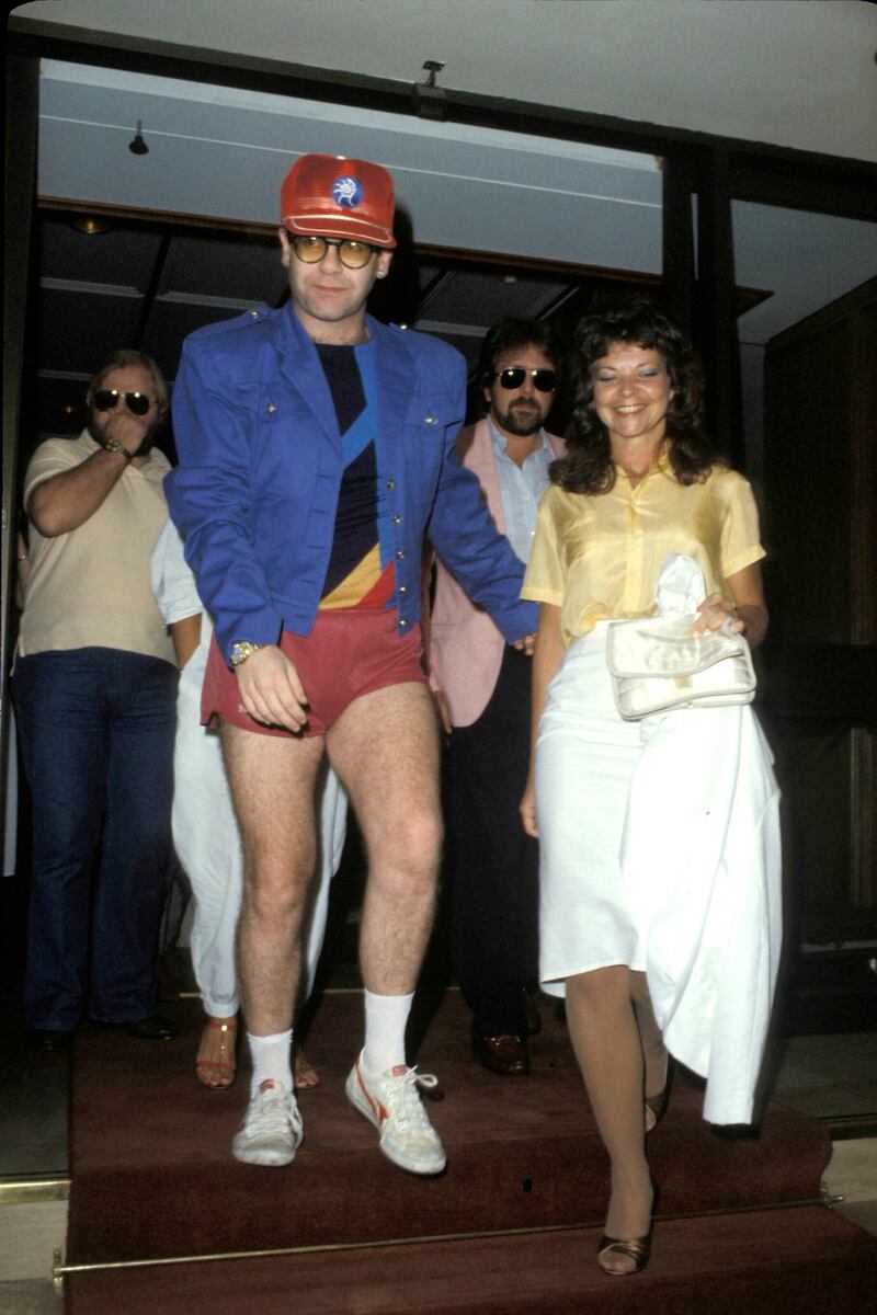 Elton John, wearing red shorts, a blue jacket and red baseball cap, with Renate Blauel following their wedding on February 14, 1984. Getty Images