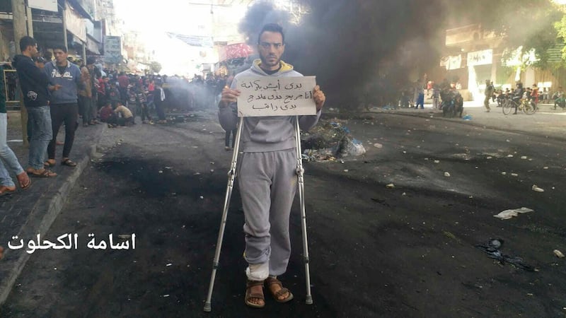 This photo provided by Palestinian journalist Osama al-Kahlout shows a protestor holding a sign that reads in Arabic, "I want to live in dignity; I'm wounded and need treatment and a salary," during a protest in Deir al Balah, central Gaza Strip, on Friday, March 15, 2019. On the left side is Al-Kahlout's name in Arabic. Al-Kahlout was detained the next day as he went live on Facebook during another protest. He said police smashed furniture, seized his belongings and beat him on the way to the police station. Hamas is facing the biggest demonstrations yet against its 12-year rule of the Gaza Strip, with hundreds of Palestinians taking to the streets in recent days to protest the dire living conditions in the blockaded territory. (Osama al-Kahlout via AP)(Osama al-Kahlout via AP)