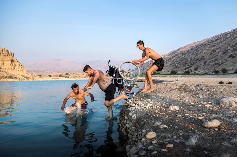 Saeed's brother and his friend push him with a chair towards the lake of Kosar Gachsaran Dam on a summer afternoon, to bring the thoughts of diving to him on Sep 9, 2020 in Gachsaran city of Kohgiluyeh and Boyer-Ahmad province, Iran.