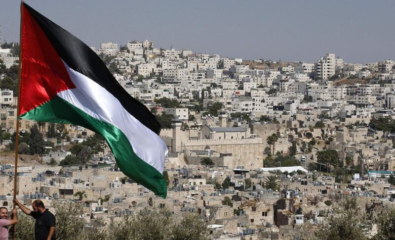 Palestinian activists from Youth Against Settlements set up a Palestinian flag overlooking the Israeli settlement of Tel Rumeida, the Ibrahimi Mosque (C), or the Tomb of the Patriarch, and the old city of the West Bank town of Hebron on September 4, 2019. Hebron is holy to both Muslims and Jews and has been a flashpoint in the Israeli-Palestinian conflict, with at least 600 Israeli settlers living under heavy military guard in the city, which is home to around 200,000 Palestinians. Before the Israeli election earlier this month, Prime Minister Benjamin Netanyahu pledged to annex West Bank settlements. / AFP / HAZEM BADER
