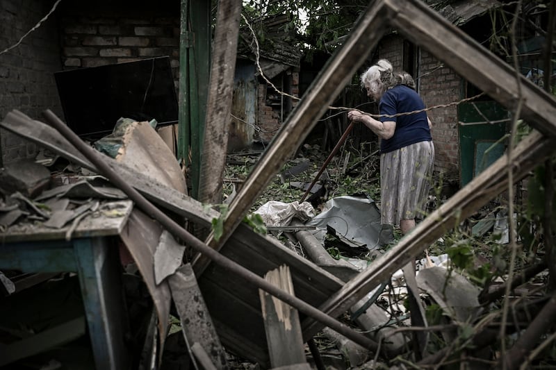 An elderly woman with a cat on her shoulder tries to clear her garden of debris after a missile strike, which killed another elderly woman in the city of Droujkivka in the eastern Ukrainian region of Donbas. AFP