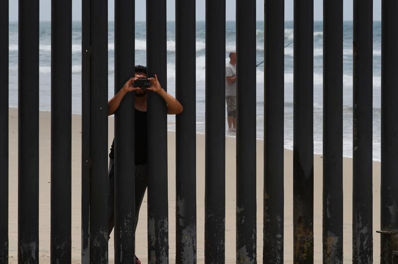 A man on the Tijuana side of the borderputs his arms through the fence while taking pictures of the beach, in San Diego. AP Photo / Jae C. Hong