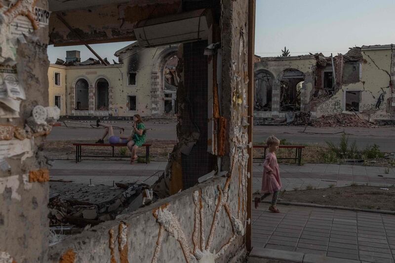 A child plays as women rest on a bench in front of destroyed residential buildings in Kostyantynivka, in eastern Donetsk, amid Russia's invasion of Ukraine. AFP