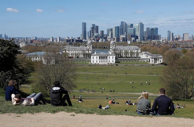 Visitors to Greenwich Park sit and look towards Canary Wharf financial district in London. Reuters