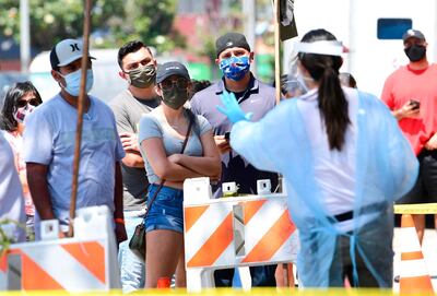 A COVID-19 test site volunteer wearing personal protective equipment gives directions to people waiting in line at a walk-in coronavirus test site in Los Angeles, California on July 10, 2020 as the state continues to set record-highs in coronavirus cases.  / AFP / Frederic J. BROWN
