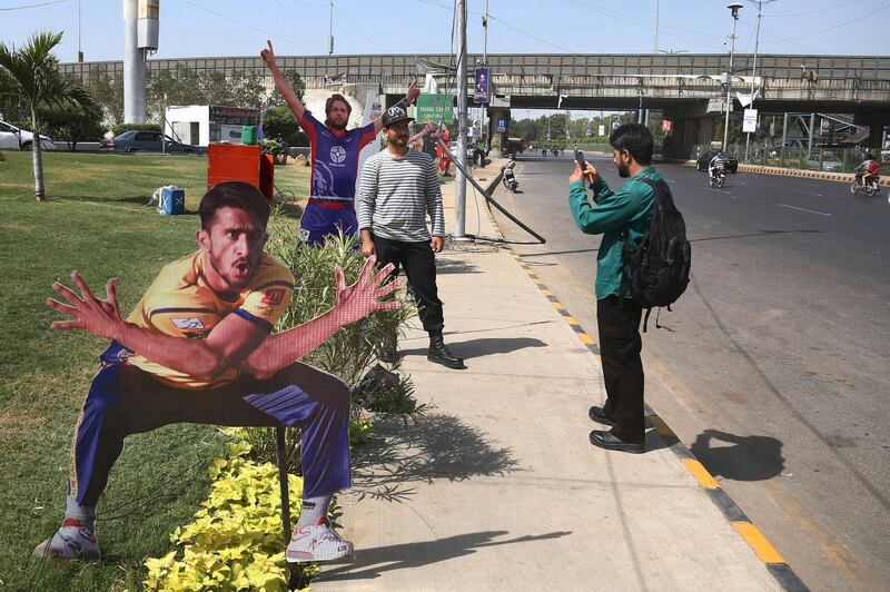 A man takes a photo of his friend standing besides a cut-out of a cricket player displayed along a roadside in preparation of the upcoming Pakistan Super League final in Karachi, Pakistan. Shakil Adil / AP Photo