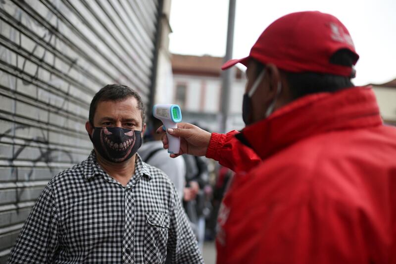 A man takes a customer's body temperature wearing a face mask before entering a shopping area, after the Colombian government decided to relax social restrictions amid the outbreak of the coronavirus disease, in Bogota, Colombia. Reuters