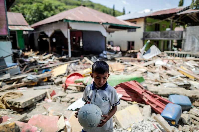 A seven-year-old boy, Taufikurahman, holds a plastic soccer ball on the rubble of a collapsed house in Donggala, Central Sulawesi, Indonesia. EPA