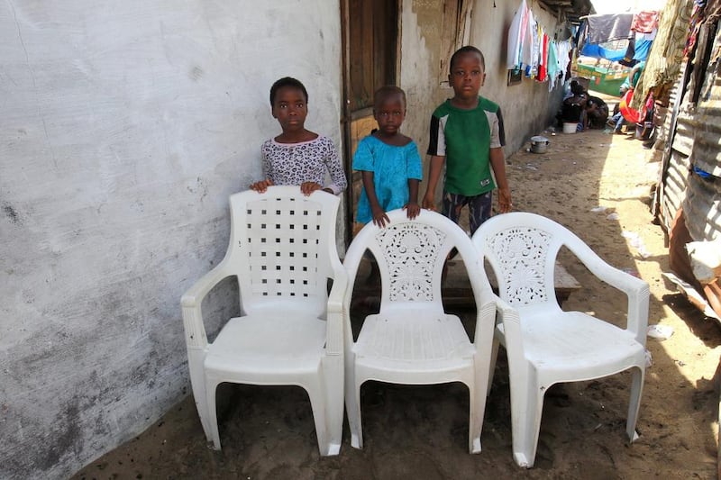 Brothers Fatu Hawa, left, Frances, centre and Raymond Risks pose for a family portrait at their home in West Point, Monrovia, Liberia. The empty chairs symbolise of their father, mother and brother who died of the Ebola virus during an outbreak of the disease in 2014.  Ahmed Jallanzo / EPA