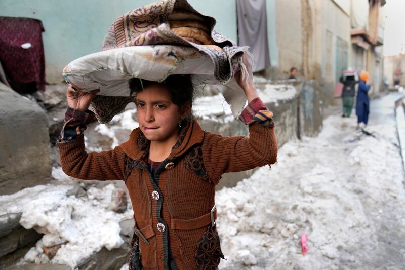 A girl carries bread on her head as she walks in the snow in Afghanistan where a humanitarian crisis is unfolding following the Taliban takeover. AP