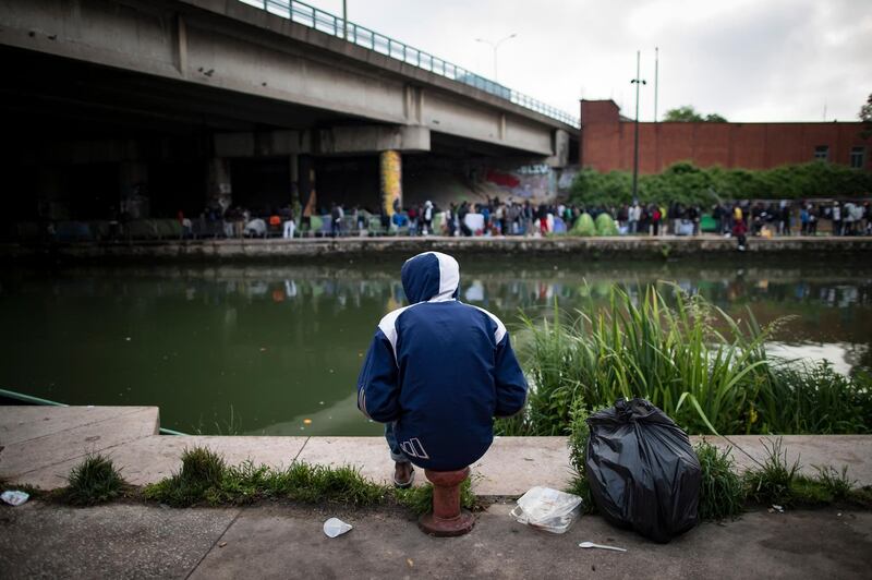 epaselect epa06772484 A migrant sits by the canal as he awaits the evacuation of a large makeshift camp along the Canal Saint Denis, in northern Paris, France, 30 May 2018. The camp, dubbed 'Millenaire' after the nearby shopping center, and home to an estimated 1,700 migrants, was peacefully cleared in a police operation which began at daybreak. The migrants boarded buses and will be relocated to shelters around the Paris area.  EPA/IAN LANGSDON