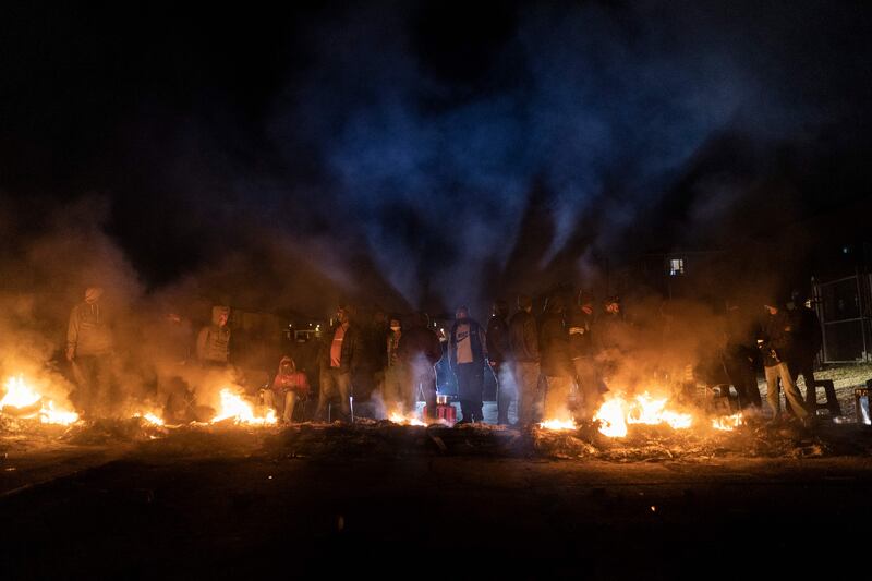 Armed community members gather around a fire to keep warm at a road block set up in Phoenix Township, North Durban, on July 15, 2021.