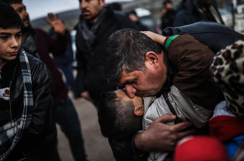 Syrian father Ali embraces one of his children, Zeyn, upon their arrival from the Syrian city of Idlib to the Turkish border. AFP / BULENT KILIC

