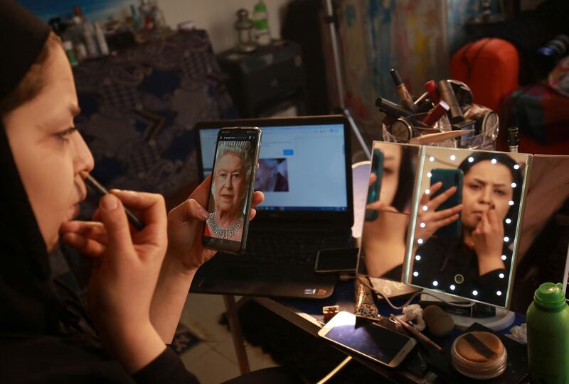 Alaa Bliha uses a portrait of Queen Elizabeth II saved on her mobile phone to work on her imitation make-up. AFP