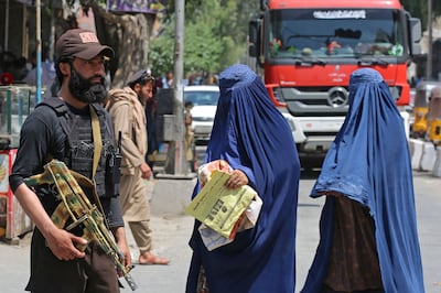Burqa-clad women walk past a Taliban security agent in Jalalabad on April 30, 2023. AFP