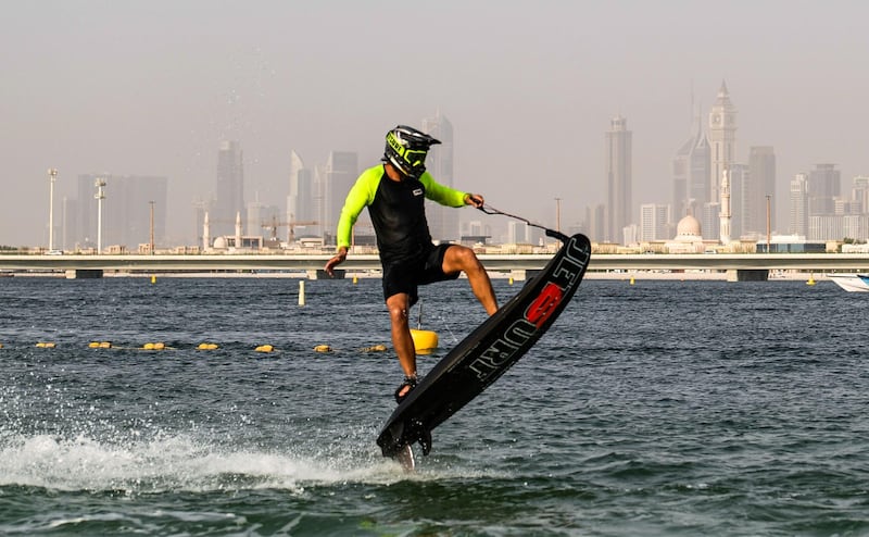 A  surfer on a jet-powered surfboard performs a stunt, with Dubai's skyline in the background.