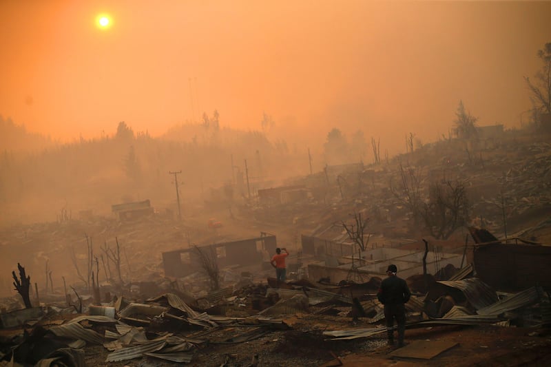 People walk amid the remains of buildings on January 26, 2017 after a forest fire in Santa Olga, 240 kilometres south of Santiago. Chile. Six people have died battling vast forest fires in central Chile, officials said Wednesday. Multiple blazes have ravaged 238,000 hectares and are growing, according to the forestry service. Pablo Vera Lisperguer / Agence France-Presse