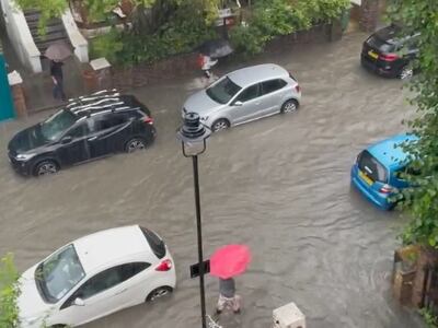 A pedestrian walks next to cars parked along a flooded street in London. Reuters