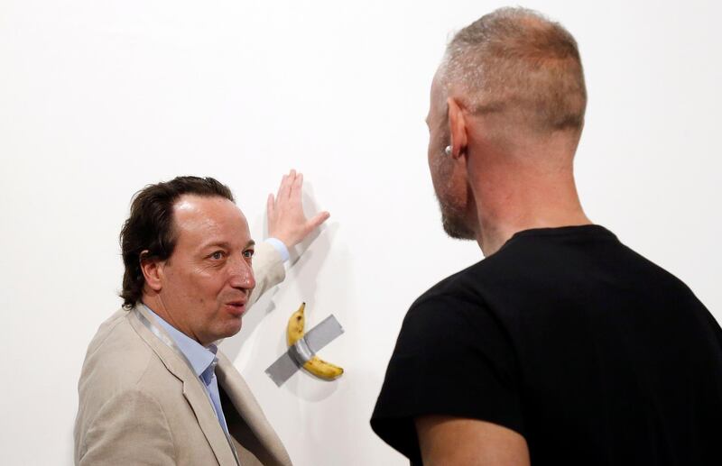 epa08047504 Emmanuel Perrotin, founder of the Perrotin Gallery (L) talks about Italian artist Maurizio Cattelan piece's 'Comedian' (a banana duct taped to the wall) with an art patron during Art Basel in Miami, Florida, USA, 05 December 2019. Art Basel represents over 250 art galleries onsite at the Miami Beach Convention Center and is considered one of the world's largest art festivals with art events throughout the city.  EPA/RHONA WISE