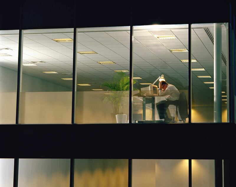 Man at desk in office, head in hands, view through window, night