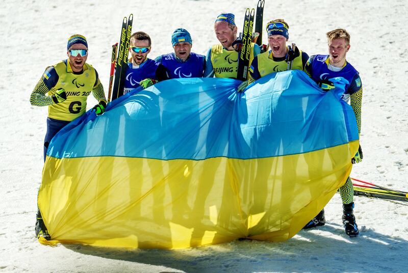 Ukrainian paralympic athletes, bronze medallist Anatolii Kovalevskyi, with guide Oleksandr Mukshyn, gold medallist Vitalii Lukianenko, with guide Borys Babar, and silver medallist Dmytro Suiarko, with guide Oleksandr Nikonovych celebrate with their country's flag after competing at the Beijing 2022 Winter Paralympic Games Para Biathlon, Men's Middle Distance Vision-Impaired event. Reuters