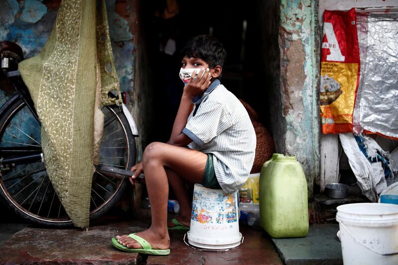 A boy wearing a protective face mask sits on a bucket outside a house in a slum area. Reuters