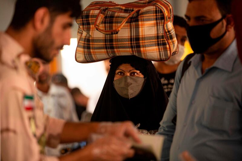 An Iraqi woman who had been stranded in Iran due to the pandemic, looks on as a soldier questions another man upon her arrival at the Al-Shalamija border crossing, west of Basra. AFP