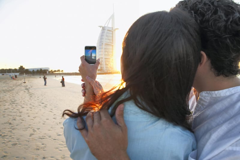 "Couple taking pictures together on beach, Dubai, United Arab Emirates"
