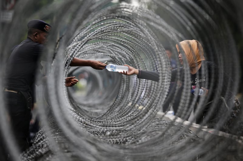 An Indonesian police officer buys a bottle of water through razor wire as he stands guard outside the Constitutional Court in Jakarta. EPA