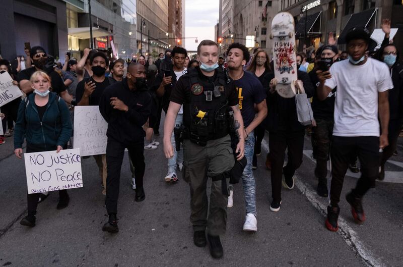 A city police officer with a Punisher path that reads 'Detroit Police' walks through a crowd of demonstartors during a protest in the city of Detroit, Michigan, on May 29, 2020, over the death of George Floyd, a black man who died after a white policeman knelt on his neck for several minutes.    Violent protests erupted across the United States late on May 29, over the death of a handcuffed black man in police custody, with murder charges laid against the arresting Minneapolis officer failing to quell boiling anger. / AFP / SETH HERALD
