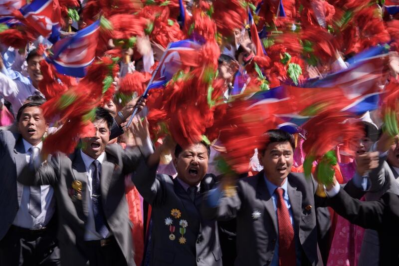 Participants wave flowers as they march past a balcony from where North Korea's leader Kim Jong Un was watching, during a mass rally on Kim Il Sung square in Pyongyang.  AFP