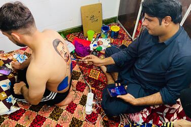 Artist Faisal Mahboob paints an image of Rashid Khan from his phone onto Rahim Sediqi's back, while the Afghan superfan watches the progress live on TikTok. Paul Radley / The National