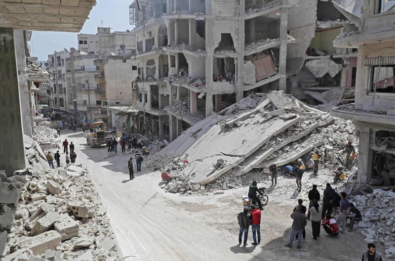 People watch as members of the Syrian Civil Defence, also known as the "White Helmets", search the rubble of a collapsed building following an explosion in the town of Jisr al-Shughur, in the west of the mostly rebel-held Syrian province of Idlib, on April 24, 2019. Over a dozen people, all but two civilians, were killed in an explosion in the jihadist-held region of Idlib in northwest Syria on Wednesday, the Britain-based Syrian Observatory for Human Rights said. The cause of the blast was not immediately clear. Idlib province is under administrative control of Hayat Tahrir al-Sham, Syria's former Al-Qaeda affiliate, with the Turkestan Islamic Party, a group of foreign jihadists from the ethnic Uighur Muslim minority, also having a large presence in the town. / AFP / OMAR HAJ KADOUR
