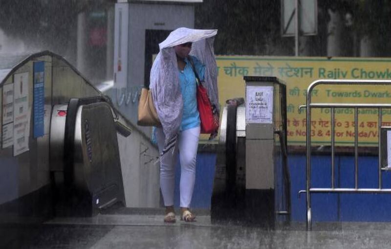 A woman is met with heavy rain as she exits the metro station in New Delhi, India.