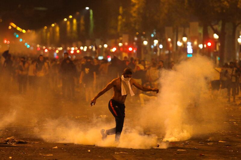 A man kicks a tear gas canister thrown by riot police during clashes on the Champs Champs Elysees avenue where soccer fans were celebrating France's World Cup victory over Croatia in Paris, France , Sunday, July 15, 2018 in Paris. France won its second World Cup title by beating Croatia 4-2. (AP Photo/Thibault Camus)