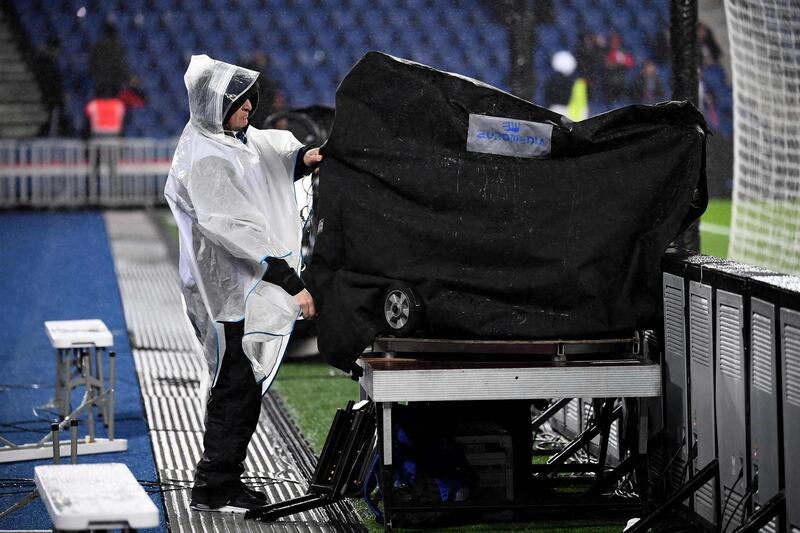 A journalist covers his equipment during heavy rain prior to the French L1 football match between Paris Saint-Germain (PSG) and Lyon (OL) at the Parc des Princes stadium in Paris.  AFP