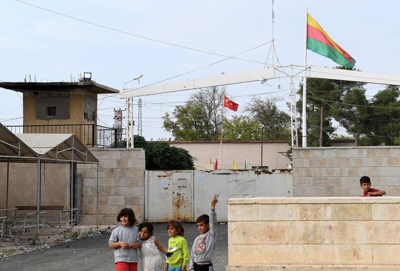 This picture taken from the Syrian Kurdish town of Kobane, along the border with Turkey in the north of Aleppo governorate, shows children standing by (foreground) a Syrian Kurdish Yellow-Red-Green Rojava flag and (background) a Turkish national flag flying across both sides of the border between Syria and Turkey.  AFP