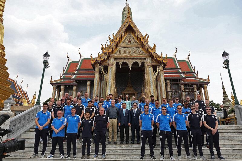 Leicester City's manager Claudio Ranieri (2nd row, centre L), owner Vichai Srivaddhanaprabha (2nd row, C) and his son and vice chairman Aiyawatt "Top" Srivaddhanaprabha (2nd row, centre R) stand along other team players and staff in front of the Emerald Buddha temple in Bangkok on May 19, 2016. - Newly crowned English Premier League champions Leicester City received a royal seal of approval at Bangkok's Grand Palace on May 19, with the team kneeling en masse in front of a portrait of the king alongside their new trophy. (Photo by STR / DAILY NEWS / AFP) / Thailand OUT