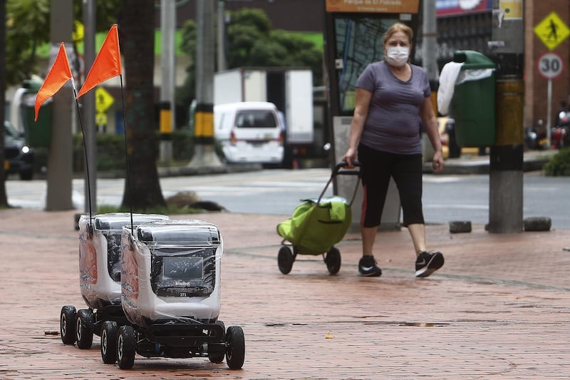 A woman observes two robots that carry home orders, in Medellin, Colombia,.  EPA