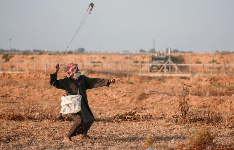 An elderly Palestinian protester wearing a surgical mask uses a slingshot to hurl stones at Israeli forces during clashes across the border following a demonstration along the fence east of Khan Yunis in the southern Gaza strip.   AFP