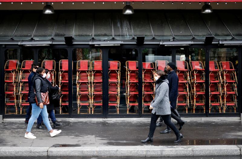 People wearing protective face masks, walk past a closed restaurant due to the restrictive measures taken to curb the spread of the Covid-19 pandemic caused by the novel coronavirus, in a street of Paris, on November 23, 2020. (Photo by Thomas COEX / AFP)