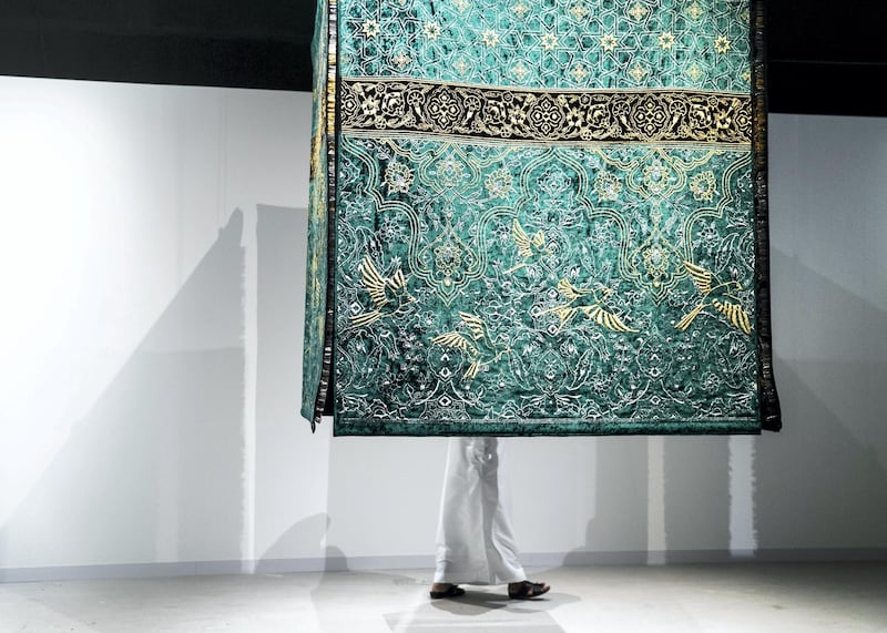 ABU DHABI, UNITED ARAB EMIRATES. 22 NOVEMBER 2019. 
 Al Burda Endowment exhibition, at the 11th edition of Abu Dhabi Art.  Visitors to Abu Dhabi Art interact with the work of Pakistani artist, Aisha Khalid. "The Garden of Love is Green Without Limit" includes a hanging fabric structure that resembles the Kaaba and its cloth cover, and the tapestry’s colour is borrowed from the dome of the Prophet’s Mosque in Medina. On the textile pieces are ornate golden visions of birds and arabesque patterns, influenced by traditional Persian carpet design. Once visitors look behind the fabric, however, they can see that this ‘embroidery’ is not made from threads, but thousands of gold-plated pins.
(Photo: Reem Mohammed/The National)

Reporter:
Section: