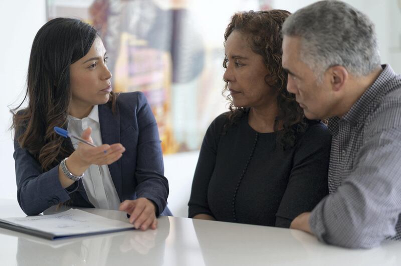 A black couple are in a meeting with their financial advisor. They are devising a financial plan to send their kids to university at their kitchen table.