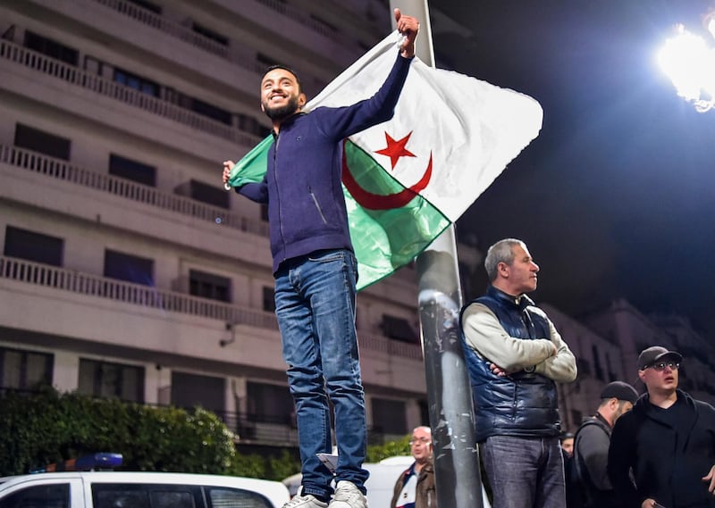 TOPSHOT - An Algerian stands with a national flag during a demonstration in the centre of the capital Algiers on March 11, 2019, after President Abdelaziz Bouteflika announced his withdrawal from a bid to win another term in office and postponed an April 18 election, following weeks of protests against his candidacy.  Bouteflika, in a message carried by national news agency APS, said the presidential poll would follow a national conference on political and constitutional reform to be drawn up by the end of 2019. / AFP / RYAD KRAMDI                        
