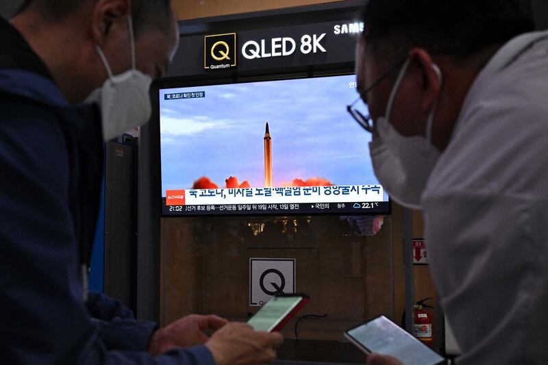 Two men check their phones as a television screen shows file footage of a North Korean missile test during a news broadcast in Seoul on May 12, 2022, after Seoul's military said it had detected three short-range ballistic missiles fired from near Pyongyang.  AFP