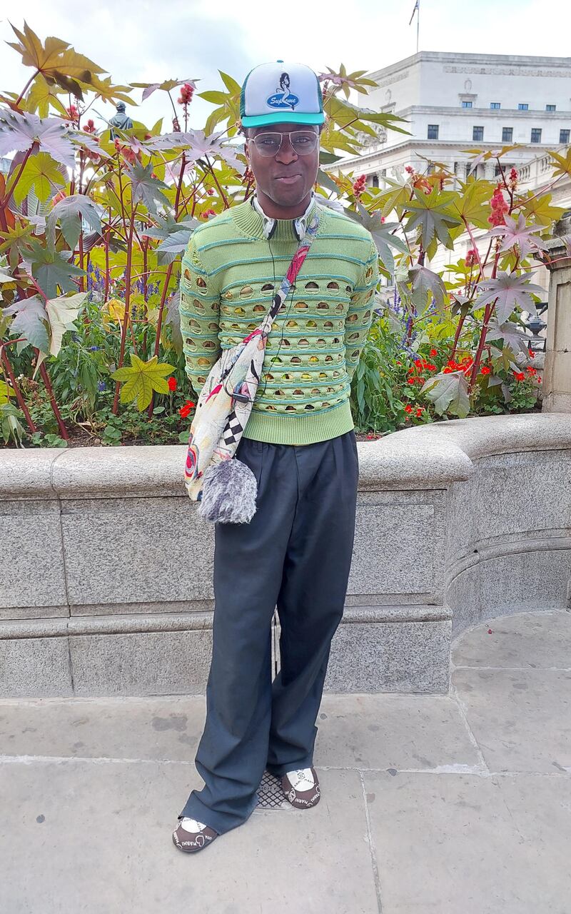 A man wears a jumper with deliberate holes, paired with a crossbody bag.
