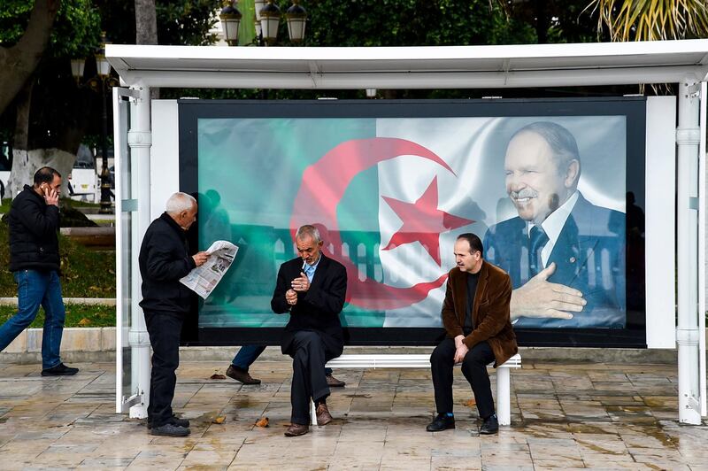 An Algerian reads a newspaper at a bus station next to a banner showing the country's flag with a portrait of President Abdelaziz Bouteflika in the capital Algiers. AFP