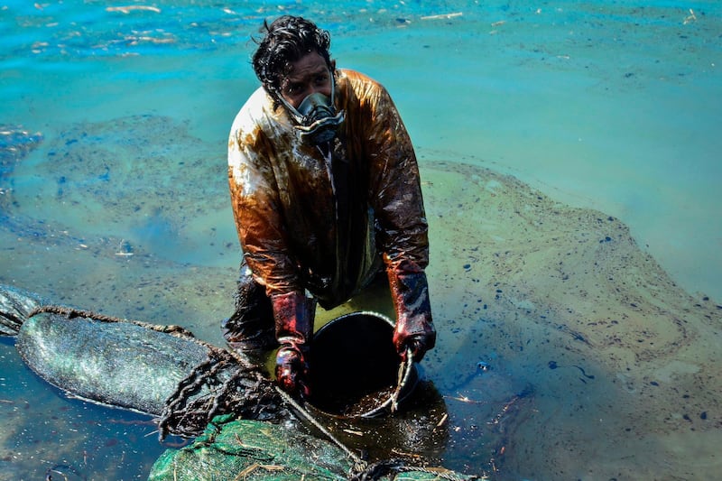 A man scoops leaked oil from the vessel 'MV Wakashio' that ran aground near Blue Bay Marine Park off the coast of Mauritius, in August, 2020.