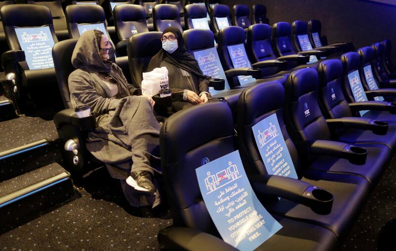 Movie viewers wearing face masks to help curb the spread of the coronavirus, as posters showing the social distancing restrictions are seen at VOX Cinema hall in Jiddah. AP Photo